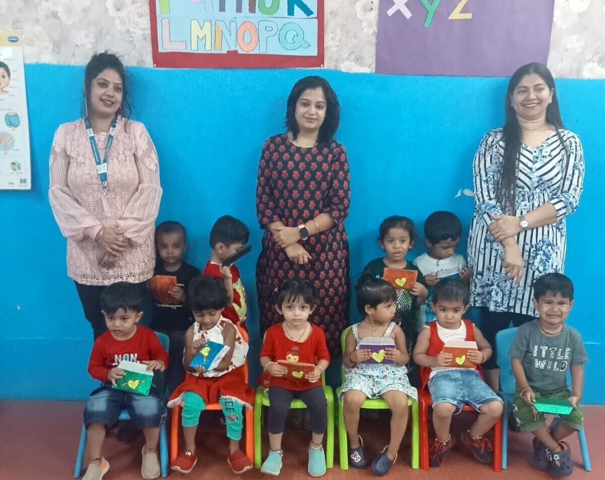 A playgroup student sitting on a chair, with teachers standing behind, providing guidance and support at Preschool in Hinjawadi.